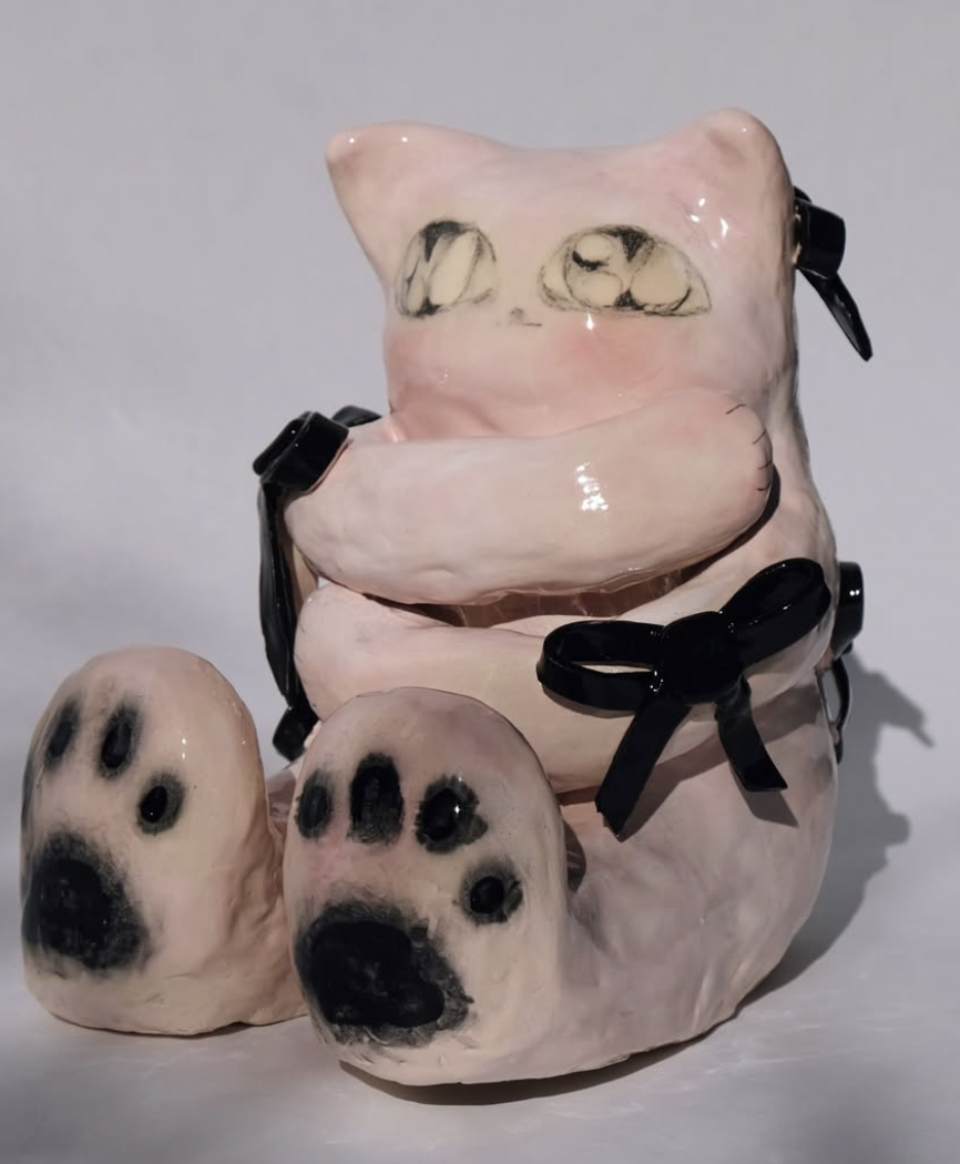 Pink ceramic cat figure with black bows and large paws