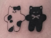 Linework tattoo of two small plush cats, one spotted and one black