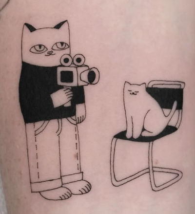 Linework tattoo of a cat holding a camera beside a seated cat
