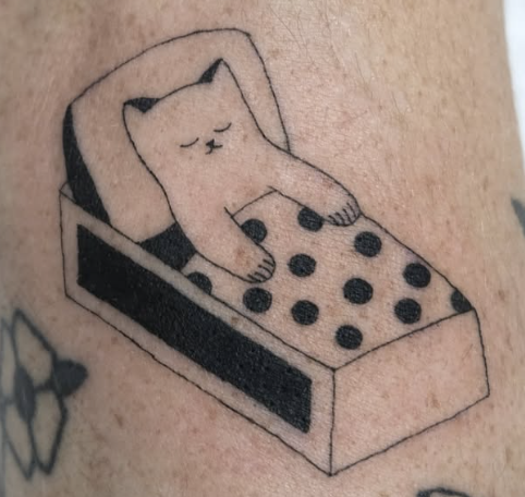 Linework tattoo of a cat sleeping in a polka-dot bed