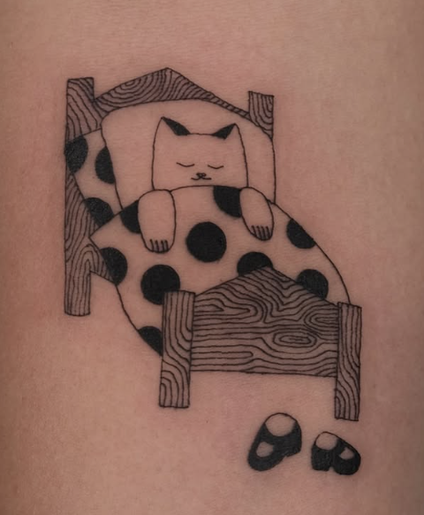 Linework tattoo of a cat asleep in a polka-dot bed