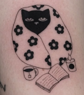 Linework tattoo of a black cat under a floral blanket with a book