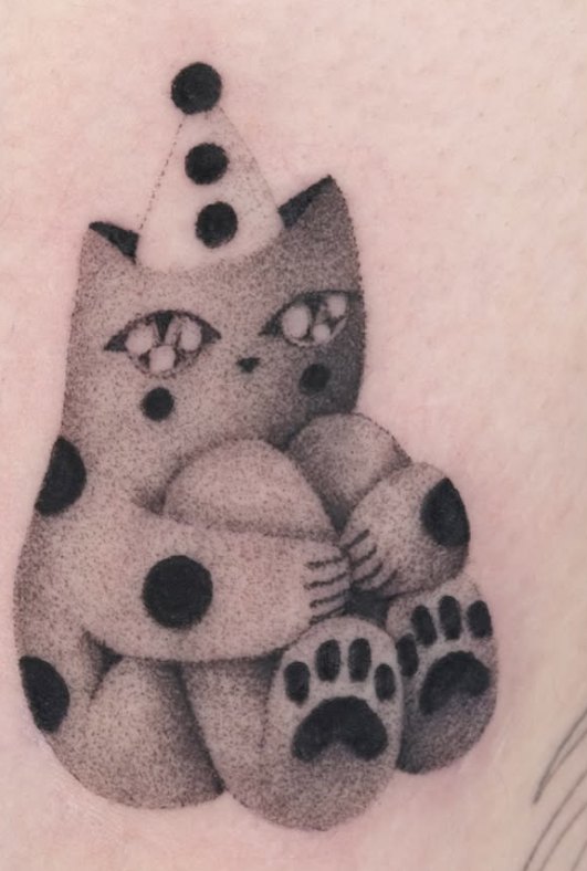Stippled tattoo of a cat in a clown hat hugging a plush toy